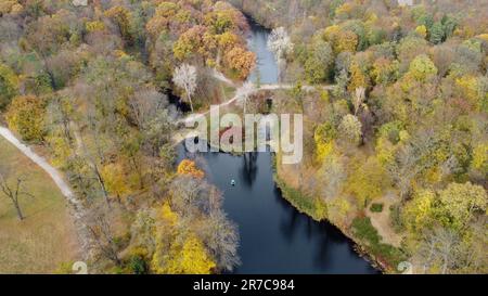 Magnifique vue sur un parc d'automne avec des arbres avec des feuilles mortes jaunes, des lacs, de l'architecture, des clairières et des personnes marchant le long des chemins de terre le jour de l'automne. Vol au-dessus du parc d'automne. Vue de dessus. Banque D'Images