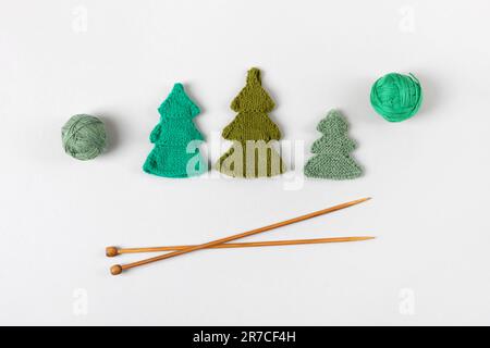 Tricotage de jouets pour les vacances d'hiver. Arbres de Noël verts tricotés avec boules de fil et aiguilles à tricoter. Jouets pour enfants. Vue de dessus, plan d'agencement. Banque D'Images