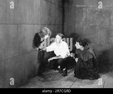 Hollywood, Californie: c. 1918 Une scène dans un premier film silencieux encore où deux hommes dans une pièce se confond avec une femme qui tient sa tête hors d'un trou dans le mur. Banque D'Images