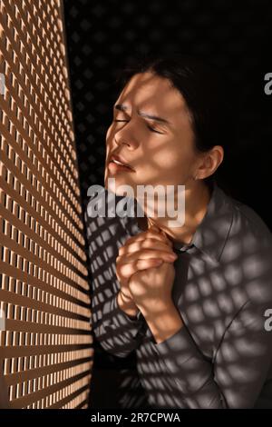 Femme priant à Dieu pendant la confession en cabine Banque D'Images