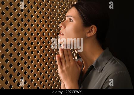 Femme priant à Dieu pendant la confession en cabine Banque D'Images