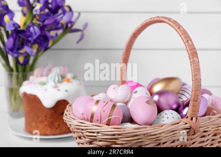 Panier en osier avec œufs de Pâques décorés avec soin sur table blanche, gros plan Banque D'Images