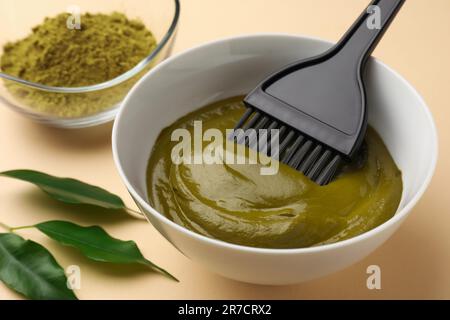 Bol de crème de henné, pinceau et feuilles vertes sur fond beige, gros plan. Coloration naturelle des cheveux Banque D'Images