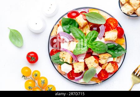 Panzanella salade de légumes italiens avec pain rassis, tomates colorées, fromage mozzarella, oignon, huile d'olive, sel et basilic vert, fond de table blanc Banque D'Images