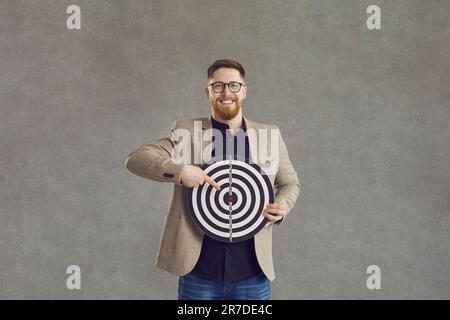 Homme d'affaires souriant tenant un tableau de fléchettes et pointant vers une prise de vue en studio Banque D'Images
