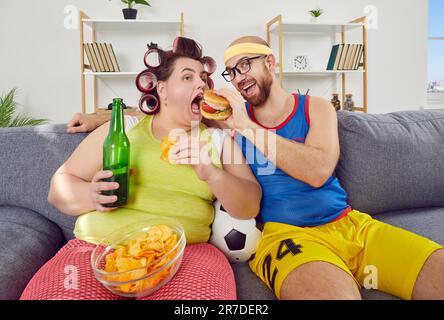 Homme drôle et femme gras ayant triché le jour, assis sur le canapé et manger des aliments malsains Banque D'Images