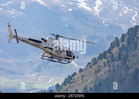 Gros plan d'un hélicoptère volant au-dessus de la forêt avec une corde de transport attachée dans les alpes suisses Banque D'Images