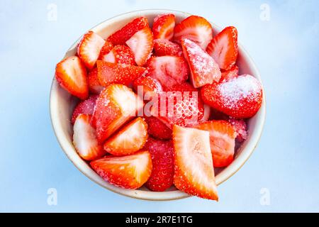 Vue rapprochée d'un bol de fraises fraîches, coupées en tranches et saupoudrées de sucre pour les faire macérer isolées sur fond blanc Banque D'Images