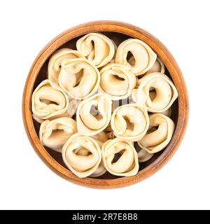 Tortellini non cuits et séchés, dans un bol en bois. Boulettes farcies fabriquées industriellement, pâtes italiennes, de forme distinctive. Banque D'Images
