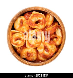 Tortellini bouilli, vêtu de sauce tomate, dans un bol en bois. Boulettes farcies fabriquées industriellement. Pâtes italiennes, faites de semoule de blé dur. Banque D'Images