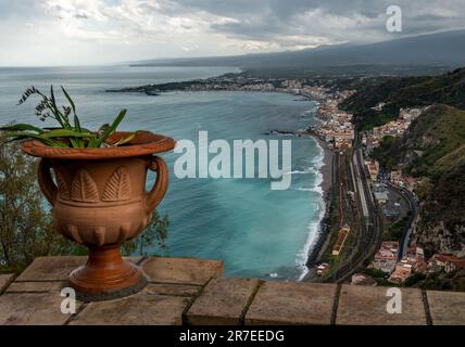 Plante florale méditerranéenne dans un pot en céramique de pierre avec vue panoramique sur le bord de mer et le volcan Etna depuis le jardin public Parco Duca di Cesaro Banque D'Images