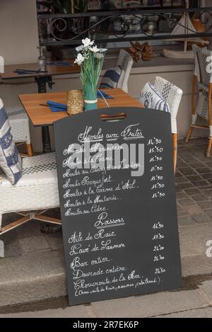 Nord de la France, Europe. UE. 2023. Tableau de menu appuyé sur une table avec des fleurs à l'extérieur d'un restaurant français. Banque D'Images