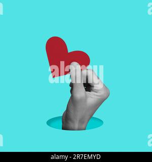 la main d'un homme en noir et blanc tenant un coeur rouge sortir d'un trou rond sur un fond bleu Banque D'Images
