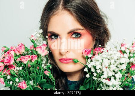 Studio photo de belle femme avec de longs cheveux foncés, maquillage rose vif, portant robe verte, tenant petit bouquet de roses Banque D'Images