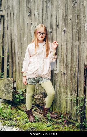 Portrait de mode extérieur de jolie petite fille, portant des lunettes, un mac rose, des collants verts et des bottes en cuir marron Banque D'Images