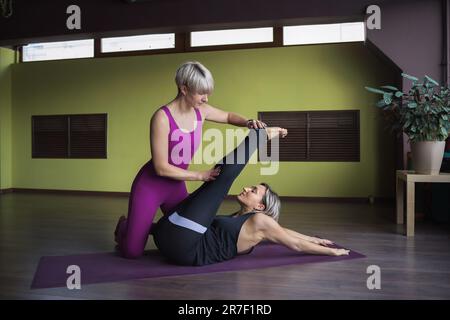 Deux femmes menant un mode de vie sain vont dans le sport, l'une aide l'autre effectuer un exercice pour étirer les muscles des jambes et du dos, s'entraîner dans Banque D'Images