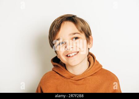 Photo studio d'un beau garçon de 10 ans aux cheveux blonds, portant un sweat à capuche marron, posant sur fond blanc, regardant vers le haut
