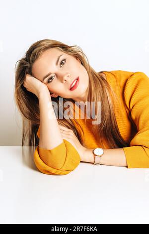 Photo de studio d'une belle jeune femme aux cheveux blonds, pull-over jaune lasse, posant sur fond blanc Banque D'Images