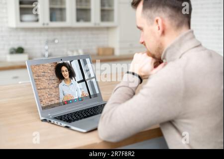 Concept d'appel vidéo. Un jeune homme parle en ligne avec une femme africaine, une collègue, discute avec un agent de soutien Banque D'Images