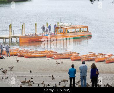 Un lancement de croisière amarré près de bateaux à rames sur la rive du lac Derwent Water, Lake District, Cumbria, Angleterre. Banque D'Images