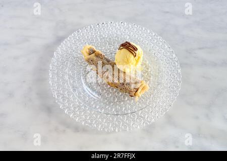 Gros plan sur une crêpe au chocolat décadente recouverte d'une grande cuillère de glace crémeuse à la vanille, servie sur une assiette blanche Banque D'Images