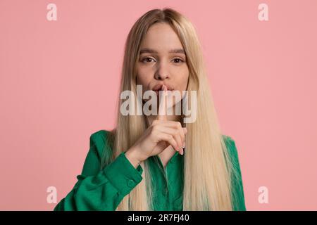 SHH silence s'il vous plaît. La jeune femme caucasienne appuie le doigt d'index sur les lèvres fait le signe de geste de silence ne dit pas secret, arrêter des potins. Jolie jeune fille isolée seule sur fond de mur de studio rose Banque D'Images