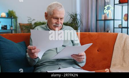 Un homme grand-père heureux travaille avec des documents de la maison, analyse de l'information, lire des documents d'affaires préparer un rapport financier à la maison. Un homme âgé gagnant choqué par la victoire soudaine bonne nouvelle de succès Banque D'Images