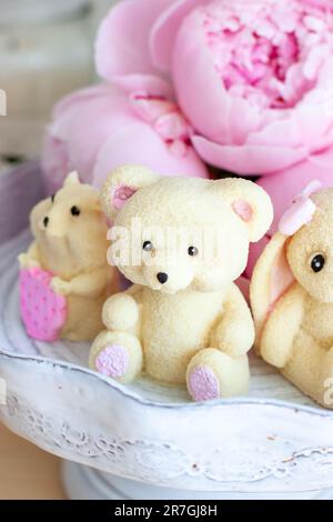 Adorable ours en peluche comestible, lapin et jouets de hamster faits de chocolat blanc avec des pivoines fraîches et des bougies sur les fonds. Cadeau pour bébé Banque D'Images