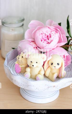 Adorable ours en peluche comestible, lapin et jouets de hamster faits de chocolat blanc avec des pivoines fraîches et des bougies sur les fonds. Cadeau pour bébé Banque D'Images