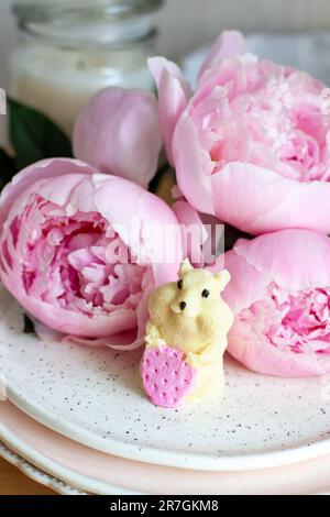 Hamster comestible fait de chocolat blanc tenant une fraise. Pivoines et bougies en arrière-plan Banque D'Images