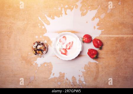 assiette avec petit déjeuner avec lait renversé, fraises, noix sur fond de bois Banque D'Images