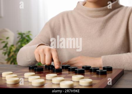 Jouer aux vérificateurs. Femme pensant à la prochaine étape à la table dans la chambre, gros plan Banque D'Images