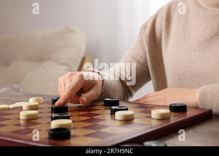 Jouer aux vérificateurs. Femme pensant à la prochaine étape à la table dans la chambre, gros plan Banque D'Images