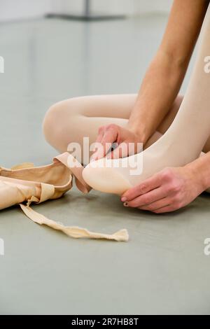 Ballerine mettant sur le ballet pointe chaussures assis sur le sol. Banque D'Images