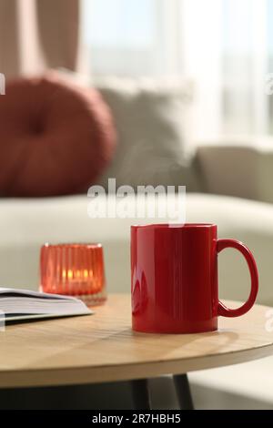 Tasse rouge, livre et bougie allumée sur table en bois à l'intérieur. Maquette pour le design Banque D'Images