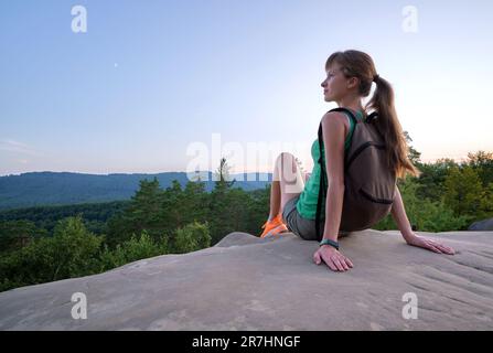 Une jeune rancheuse se reposant sur le sommet d'une montagne rocheuse en profitant de la nature matinale pendant son voyage sur un sentier sauvage. Une femme seule qui traverse une colline Banque D'Images