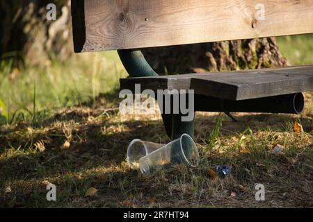 Banc en bois dans un parc par une chaude journée d'été et plusieurs tasses en plastique dispersées sur le sol. Plastique, pollution de l'environnement Banque D'Images