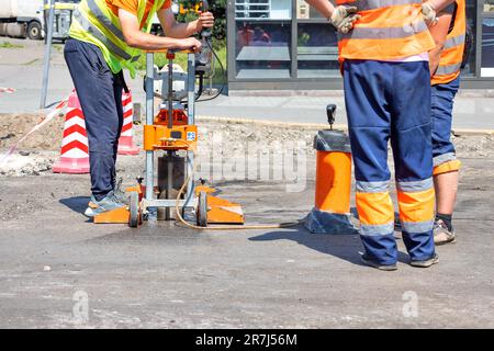 Les travailleurs de la route en capes réfléchissantes forent de l'asphalte avec une machine de carottage pour prendre et mesurer des carottes pendant les réparations sur route par temps ensoleillé. Copier l'espace. Banque D'Images