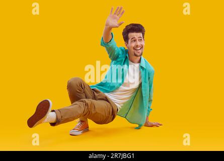 Portrait d'un jeune homme barbu joyeux dansant sur le sol et agitant la main sur fond jaune. Banque D'Images