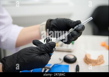 Gros plan des mains du dentiste médecin dans des gants médicaux stériles noirs, tenant la seringue pour l'anesthésie dentaire locale. Dentisterie Banque D'Images