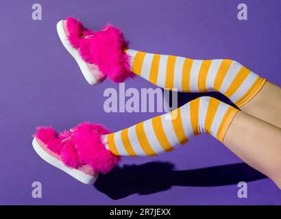Vue latérale d'une femelle anonyme avec ombre des jambes relevées dans des chaussettes longues de couleur jaune et des chaussures de fuchsia roses tout en étant assis sur fond violet Banque D'Images