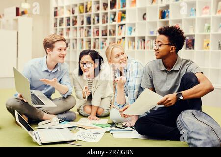 Groupe de jeunes étudiants assis à la bibliothèque et discutant des idées pour un projet conjoint Banque D'Images