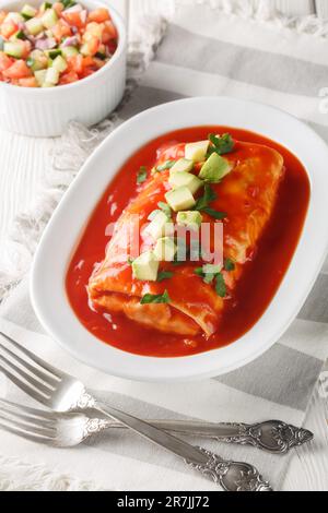 Burrito humide farci de viande déchiquetée, haricots, riz et fromage, étouffé dans la sauce enchilada rouge sur l'assiette sur la table en bois. Verticale Banque D'Images