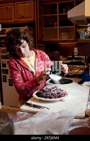 Une jeune fille de treize ans verse du sucre sur une tarte aux baies maison dans un chalet en Ontario, au Canada. Banque D'Images