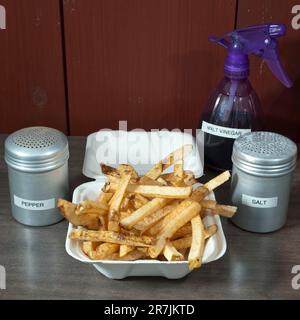 Tous les ingrédients clés pour obtenir des frites parfaites (frites) sont placés sur le comptoir d'un camion à frites local, de frites coupées à la main, de salières et poivrières et de vinaigre de malt dans une bouteille vaporisée, à Elm Banque D'Images