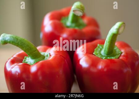 Trois poivrons rouges biologiques sont regroupés sur un comptoir en bois dans une cuisine de Seattle, Washington. Banque D'Images