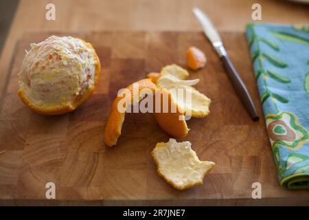 Une orange partiellement pelée est posée sur une planche à découper en bois sur un comptoir. Banque D'Images