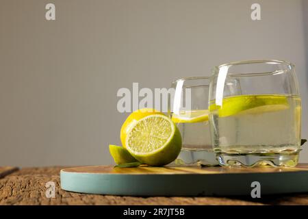 Gros plan de limonade dans des verres à boire avec des tranches de citron sur la planche à découper sur fond gris Banque D'Images