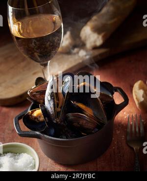 Moules marinière, moules au vin blanc, sur une table en bois avec un verre de vin blanc. Banque D'Images