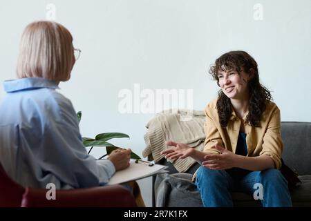 Jeune femme souriante parlant à un thérapeute pendant qu'elle prend des notes dans le document pendant la session psycho Banque D'Images